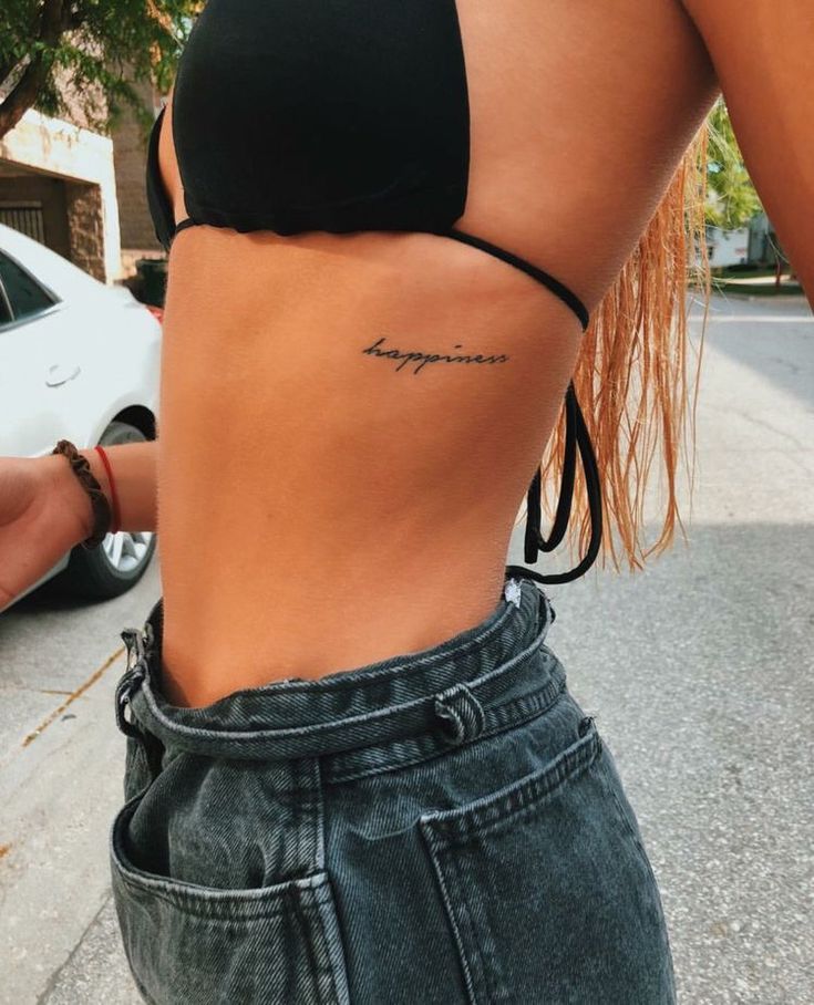 a woman with a tattoo on her lower back and the word happiness written in cursive writing