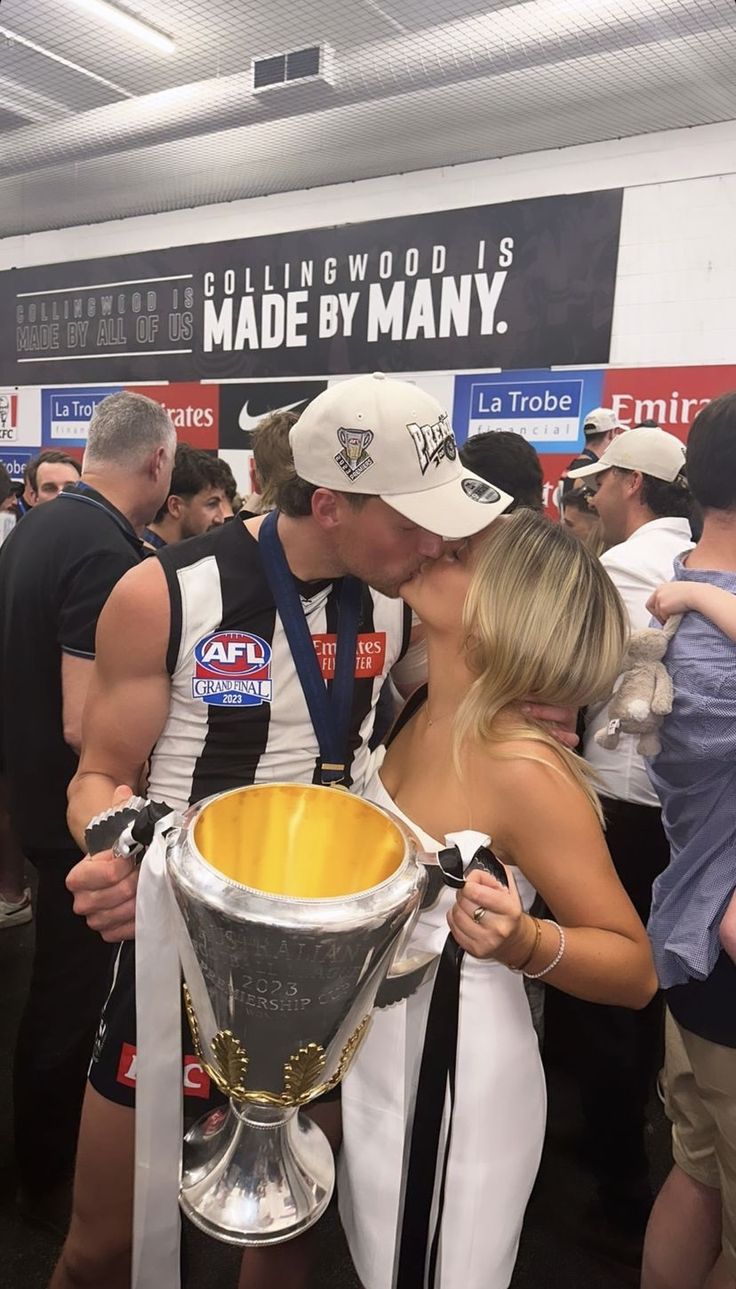 a man and woman kissing each other in front of a trophy at a sporting event