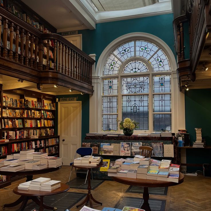 a library filled with lots of books next to a large stained glass window covered in windows