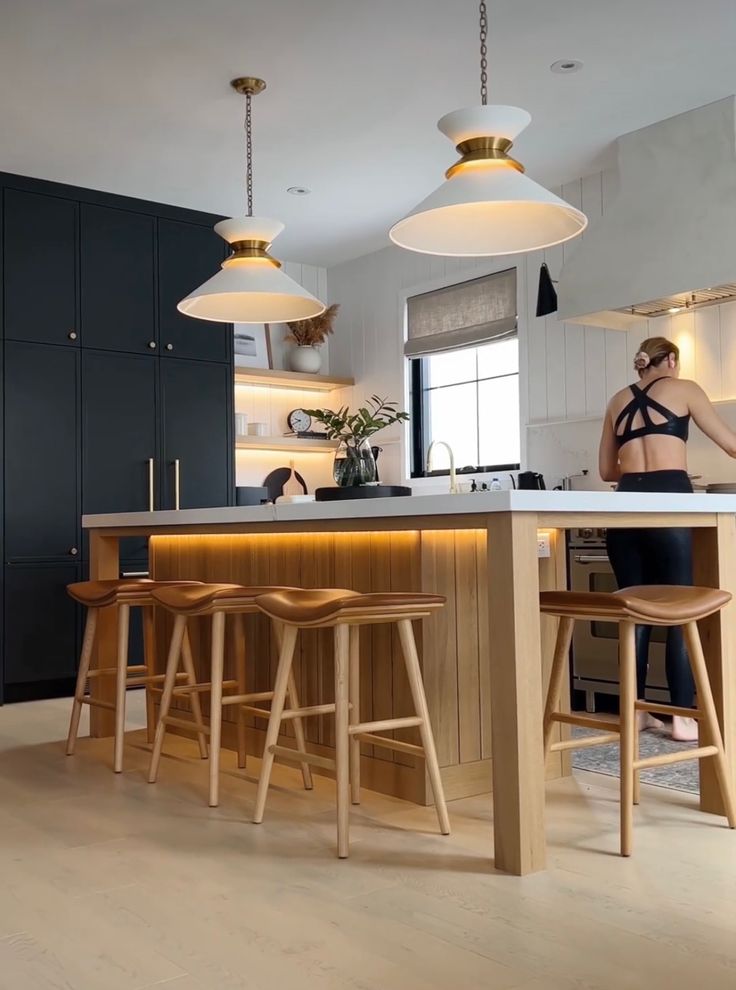 a woman is standing at the kitchen island with stools in front of her and two lights hanging from the ceiling