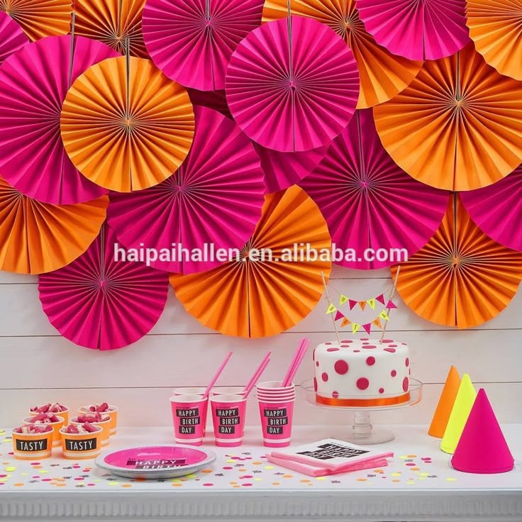 pink and yellow paper fans hanging on the wall above a table with cupcakes