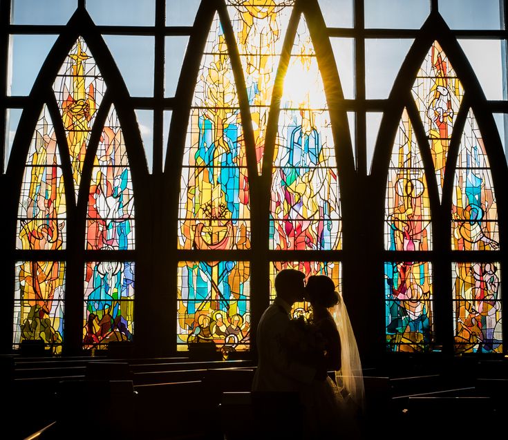 a bride and groom kissing in front of stained glass windows