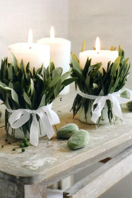 two white candles sitting on top of a wooden table next to flowers and leaves in vases