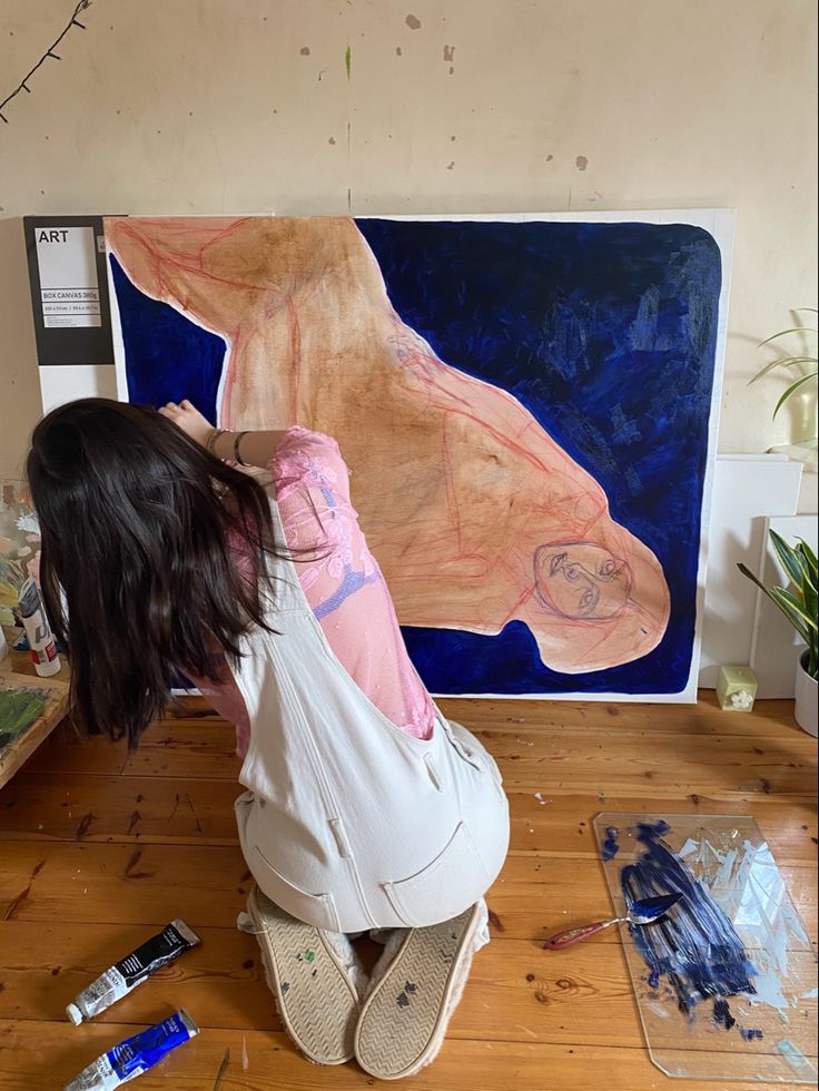 a woman sitting on the floor in front of a large painting with her head down