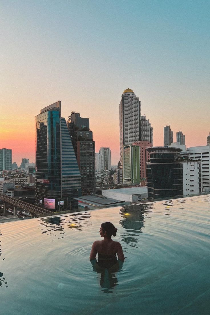 a woman sitting in the middle of a swimming pool with city buildings in the background