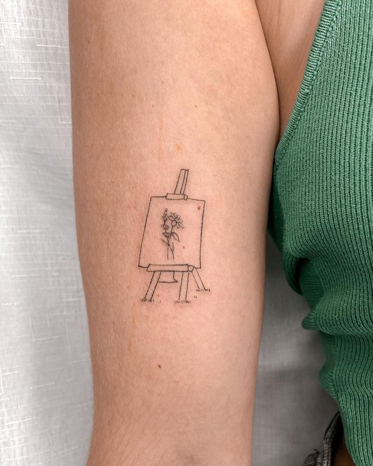 a woman's arm with a small drawing easel on it and a flower