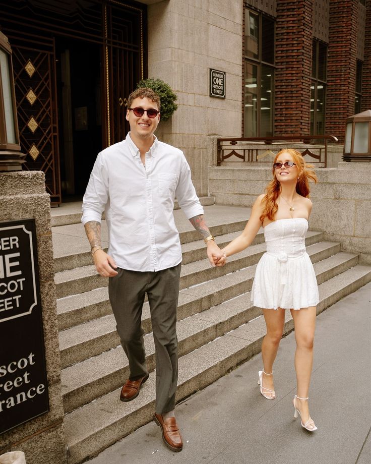 a man and woman holding hands while walking down the street