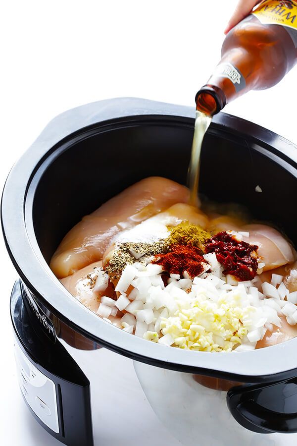 someone is pouring sauce into an electric crock pot filled with meat, rice and vegetables