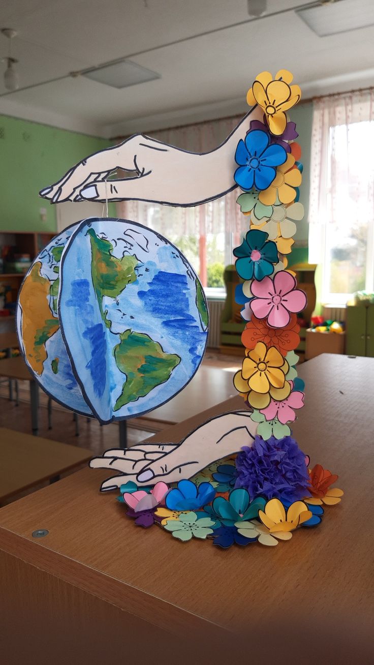 a sculpture made out of paper flowers and hands holding the earth on top of it