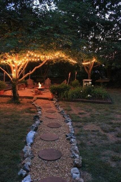 a stone path in the middle of a yard with lights strung over it and trees