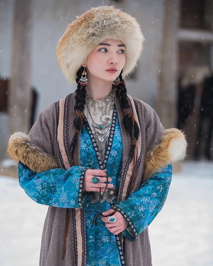 a woman wearing a fur hat standing in the snow with her hands on her hips