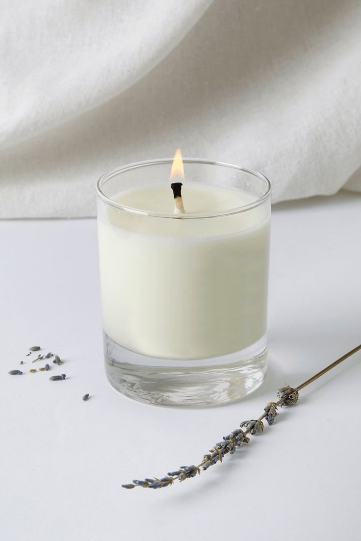 a candle is sitting on a table next to some dried lavenders and a white cloth