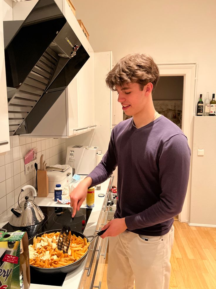 a young man standing in front of a pan of food on top of a stove