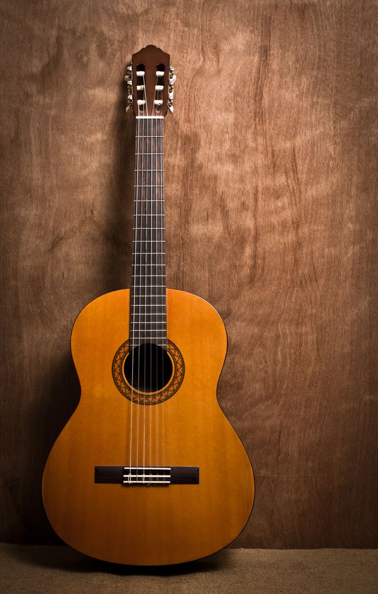 an acoustic guitar sitting on top of a wooden table next to a brown wall and wood paneling