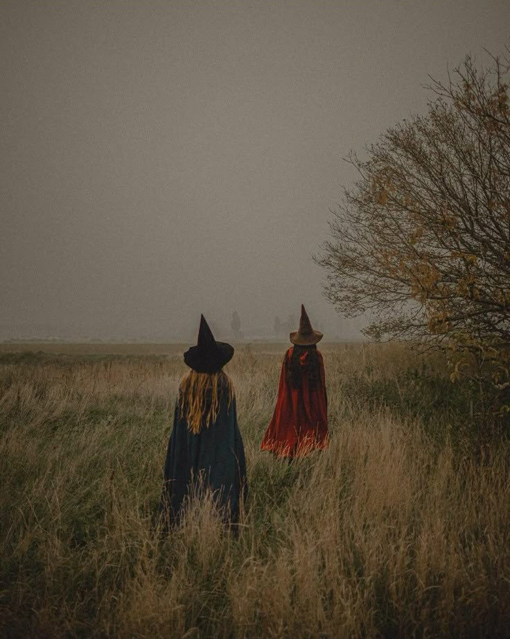 two people in witches costumes walking through tall grass