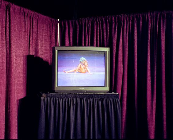 a tv sitting on top of a table in front of a purple curtain with a woman naked