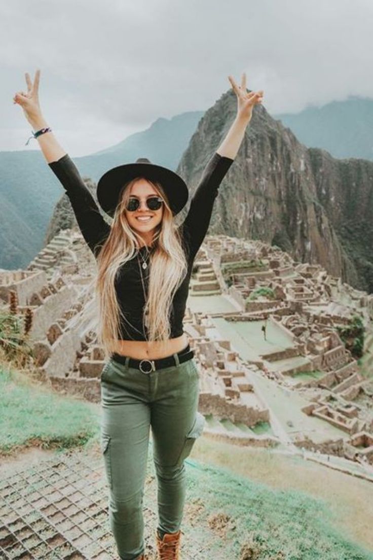 a woman standing on top of a mountain with her arms in the air and smiling