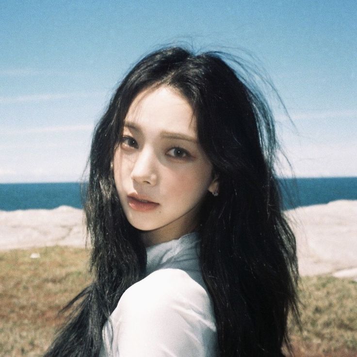 a woman with long black hair standing in front of the ocean