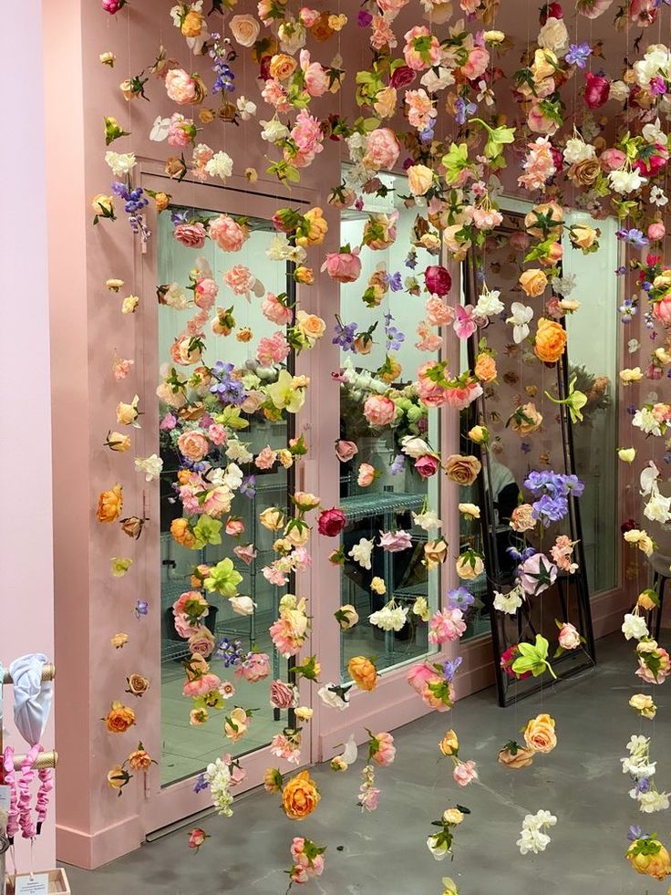 a room filled with lots of fake flowers hanging from the ceiling next to glass doors