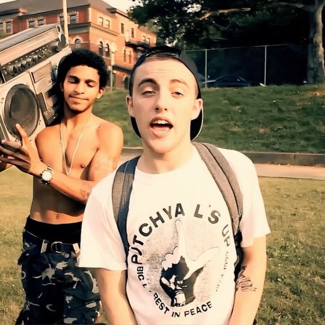 two young men standing next to each other in the grass with an old radio on their shoulders