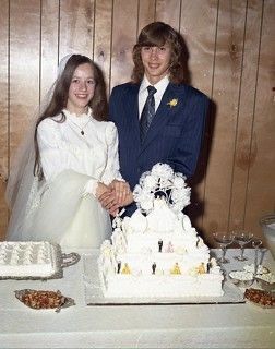 two people standing next to each other in front of a cake