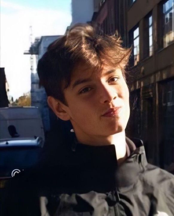 a young man standing in the middle of a street next to tall buildings and looking off into the distance