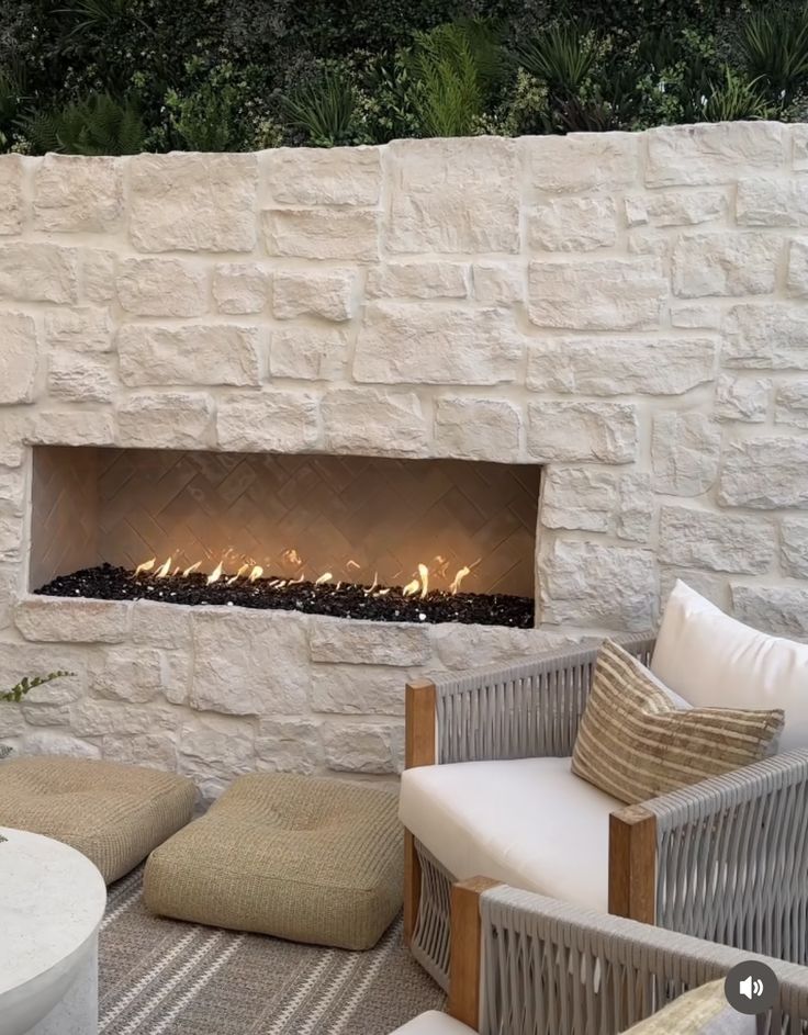 an outdoor fireplace in the middle of a patio with wicker furniture and pillows on it