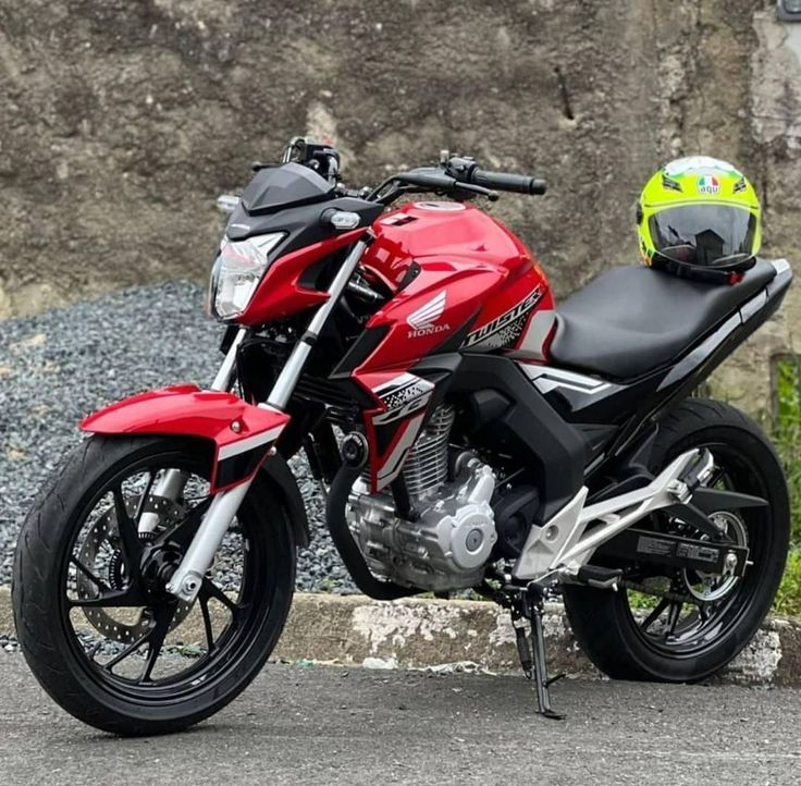 a red and black motorcycle parked next to a large rock wall with a helmet on it's back end