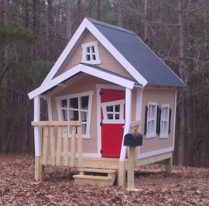 a small house with a red door and porch in the middle of leaf covered ground