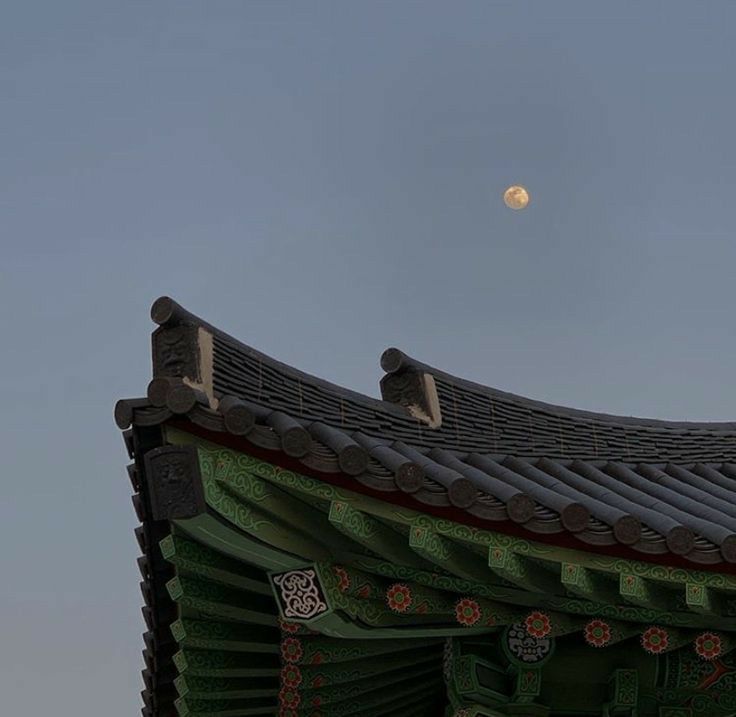 a full moon is seen in the sky above a building with roof tiles and decorations