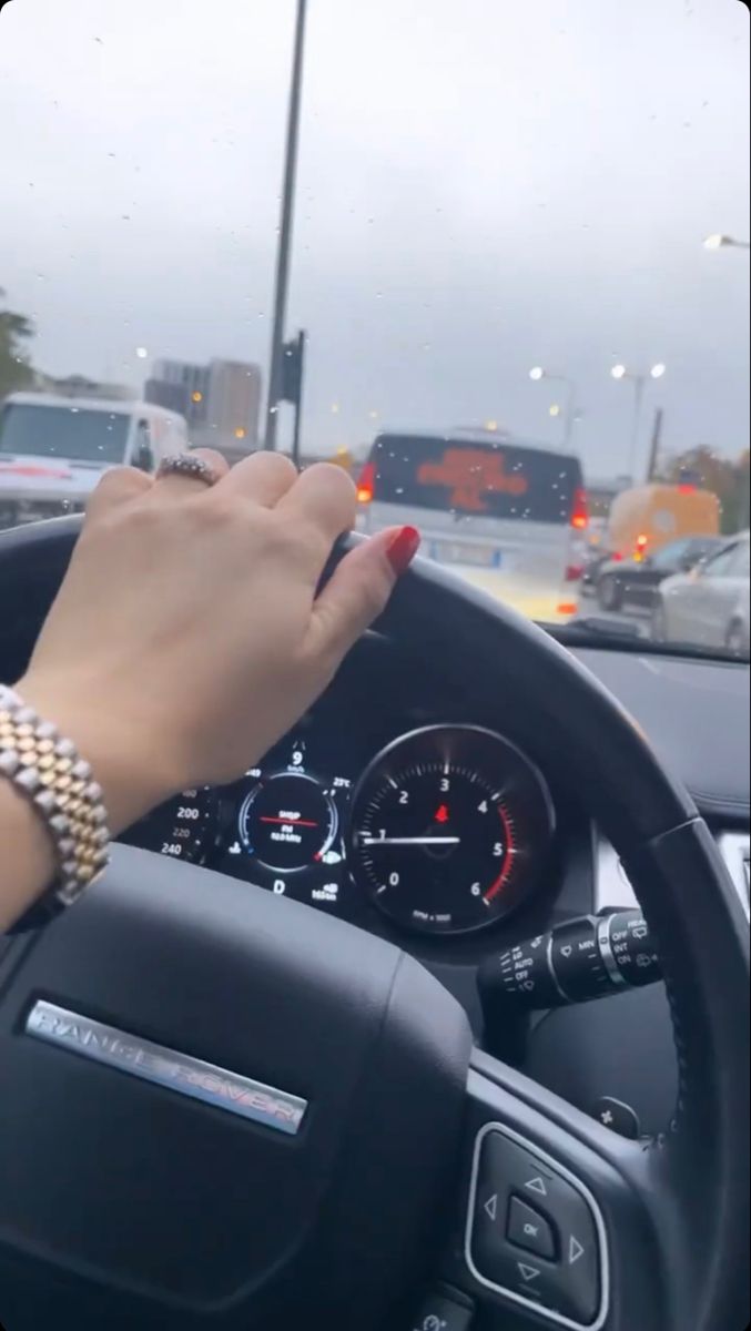 a woman is driving her car on the street with traffic lights in the back ground