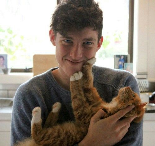 a young man holding a cat in his arms and smiling at the camera while he holds it up to his face