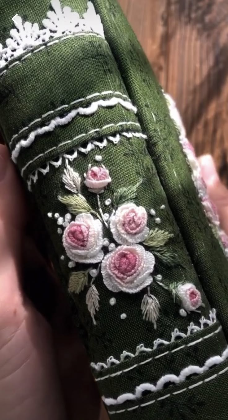 someone is holding an old green case with pink roses and white lace on the sides