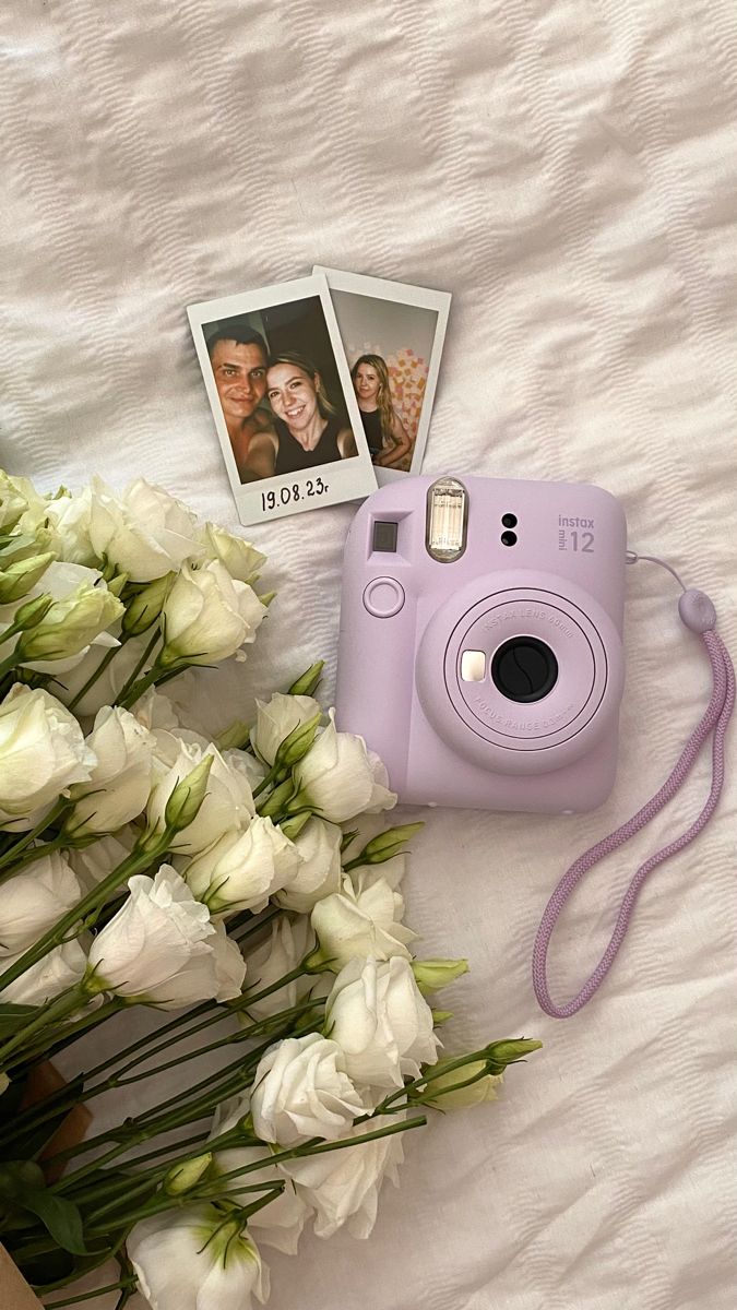 a pink camera and some white flowers on a bed next to two polaroid pictures