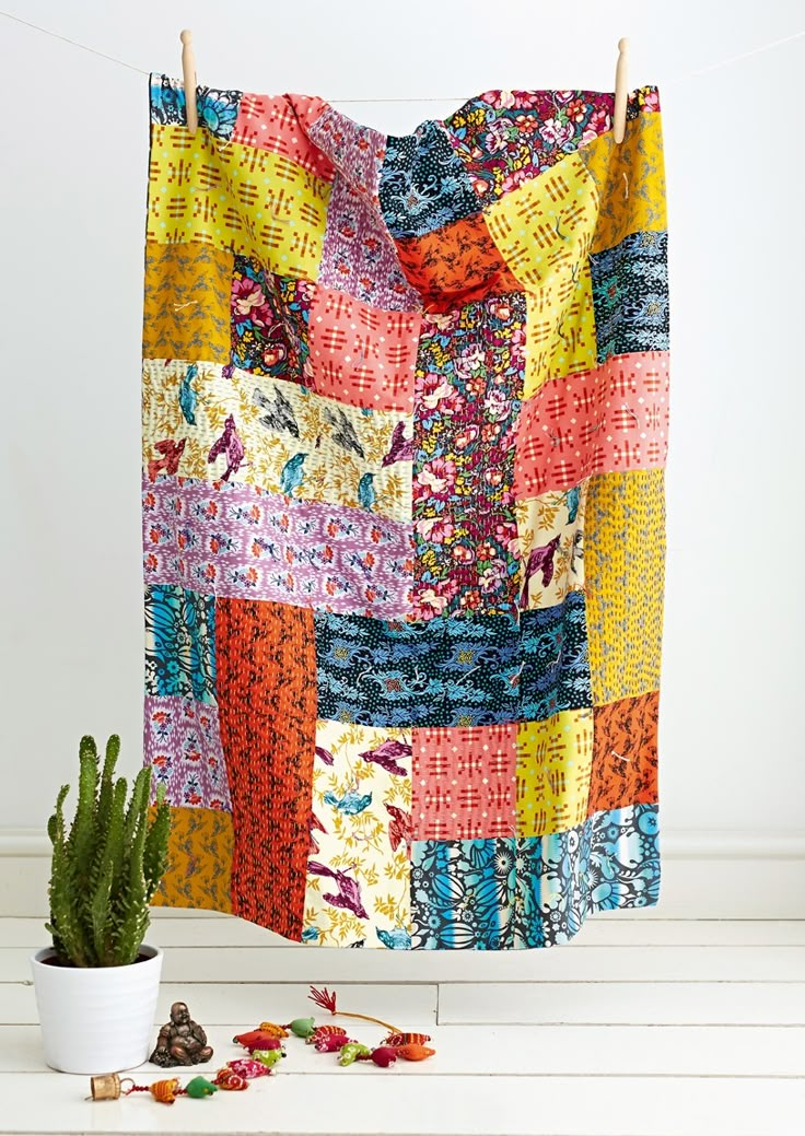 a colorful quilt hanging on a clothes line next to a potted plant and cacti