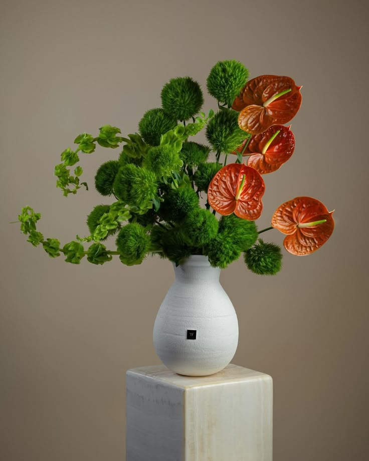 a white vase filled with lots of flowers on top of a wooden block in front of a wall