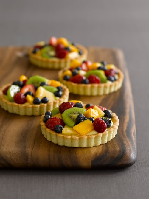 three fruit tarts sitting on top of a wooden cutting board