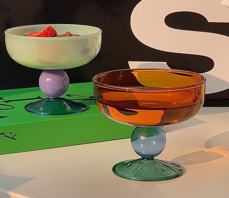 two glasses sitting on top of a table next to each other with fruit in them