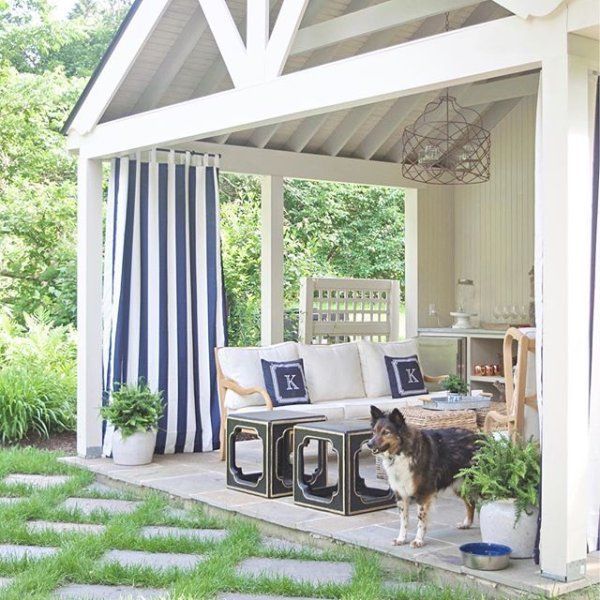 a dog is standing on the patio in front of an outdoor living area with blue and white striped curtains