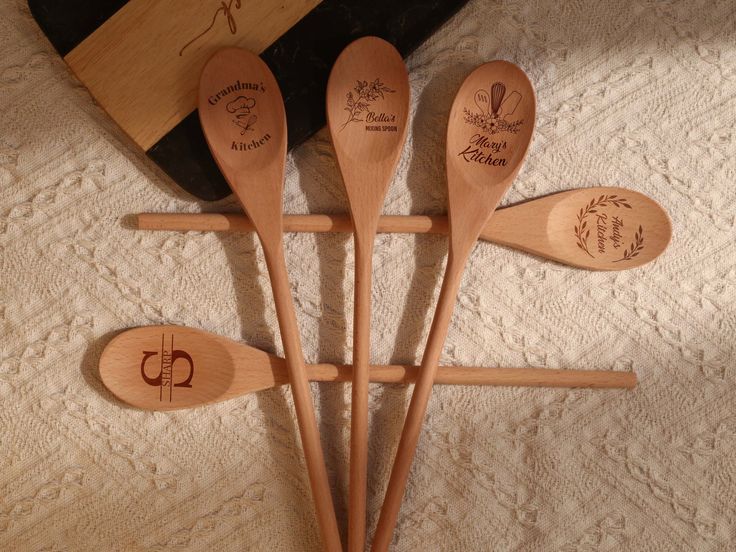 four wooden spoons with engraved names on them sitting next to a bag and purse