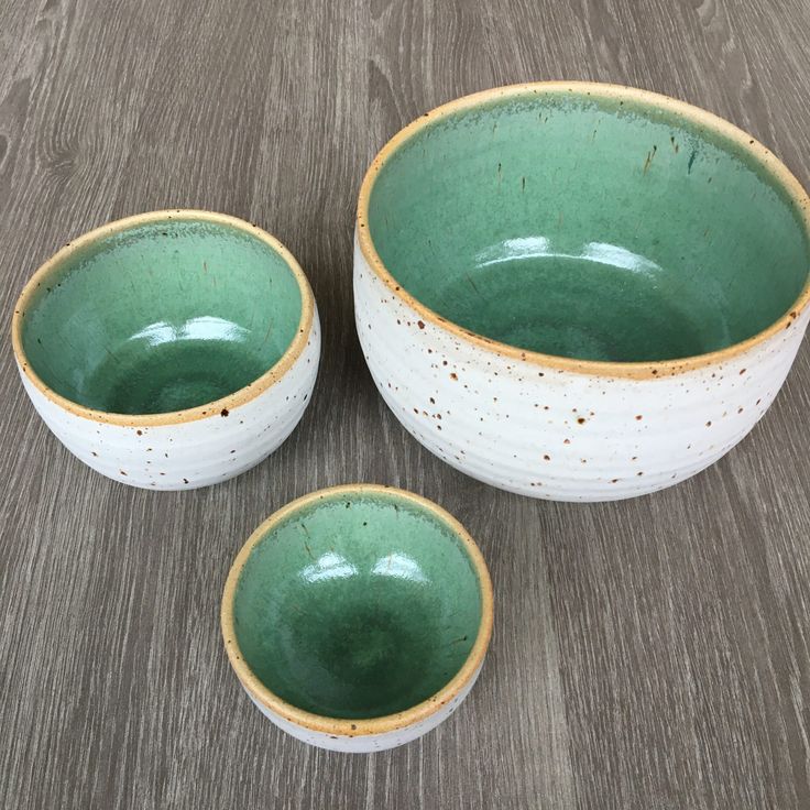 three green and white bowls sitting on top of a wooden table