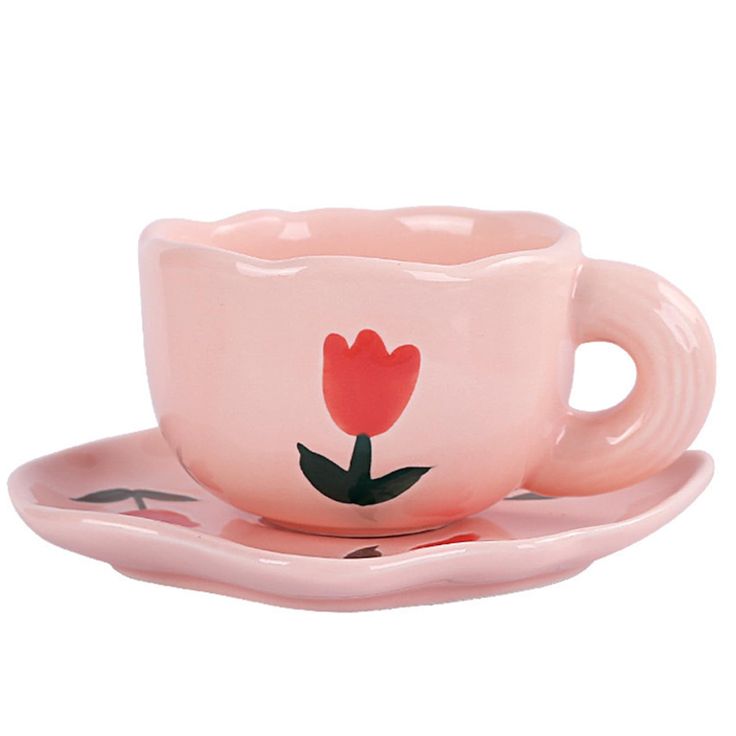 a pink cup and saucer with a flower painted on the side sitting on a plate