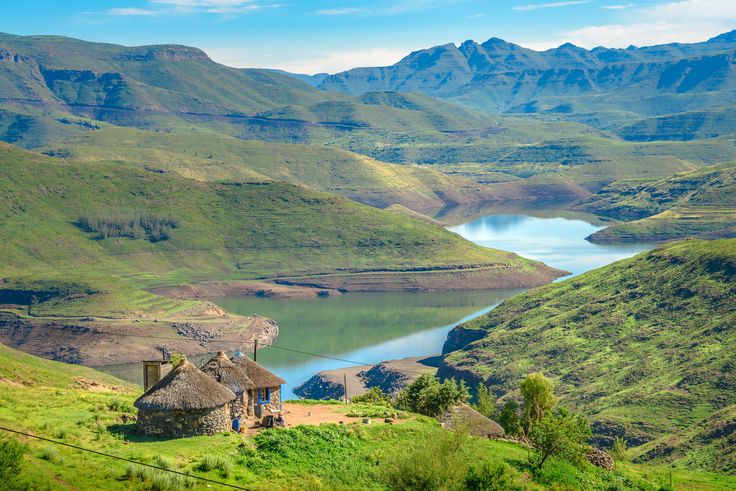 an old thatched house in the middle of a green valley with mountains around it