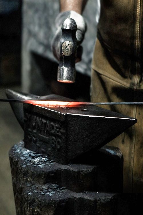 a man is working on an iron with a hammer in his hand and red hot flame coming out of it