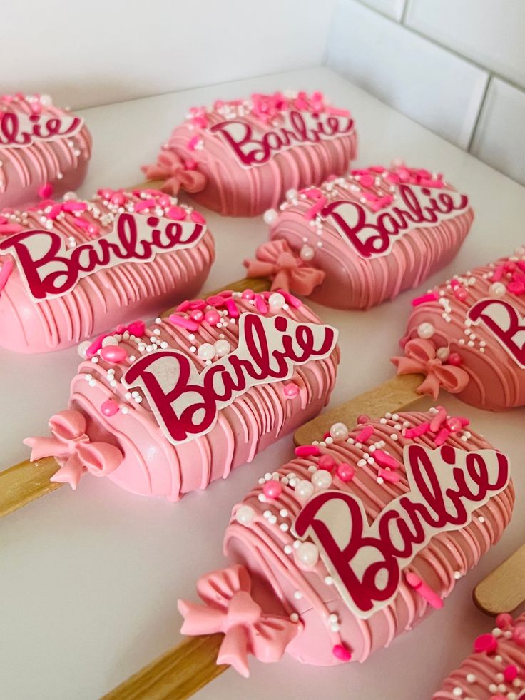 pink and white cake pops with name on them sitting on a table next to wooden utensils