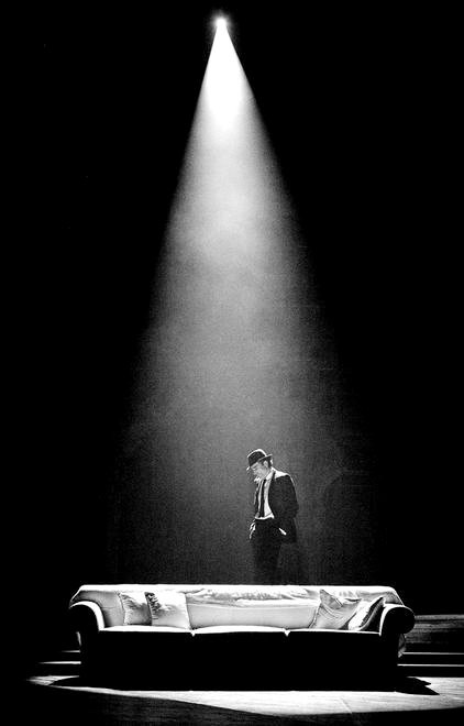 a black and white photo of a man standing in front of a bed on stage