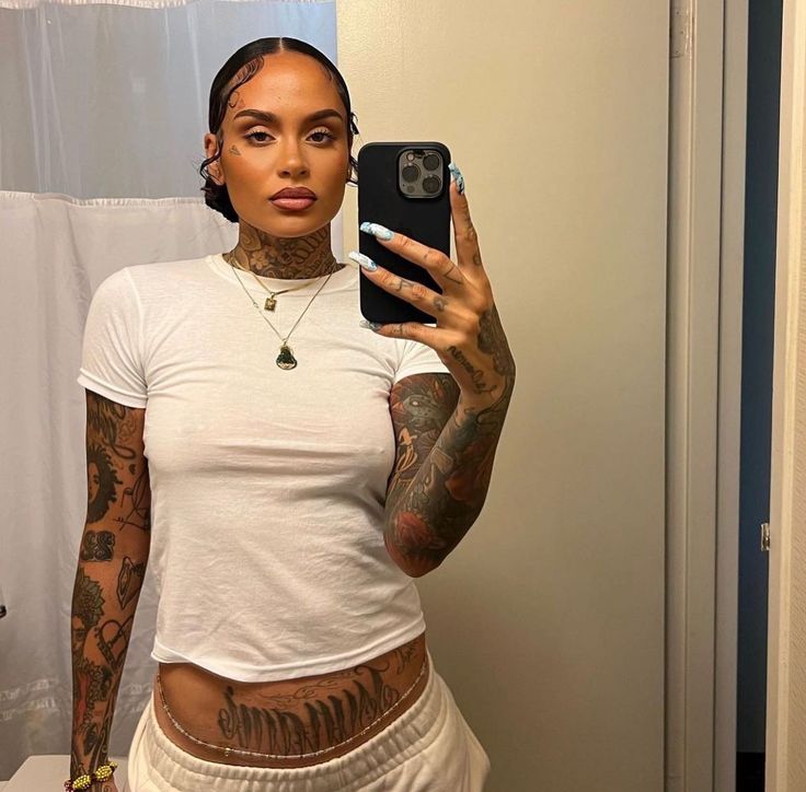 a woman with tattoos taking a selfie in the bathroom while holding a cell phone