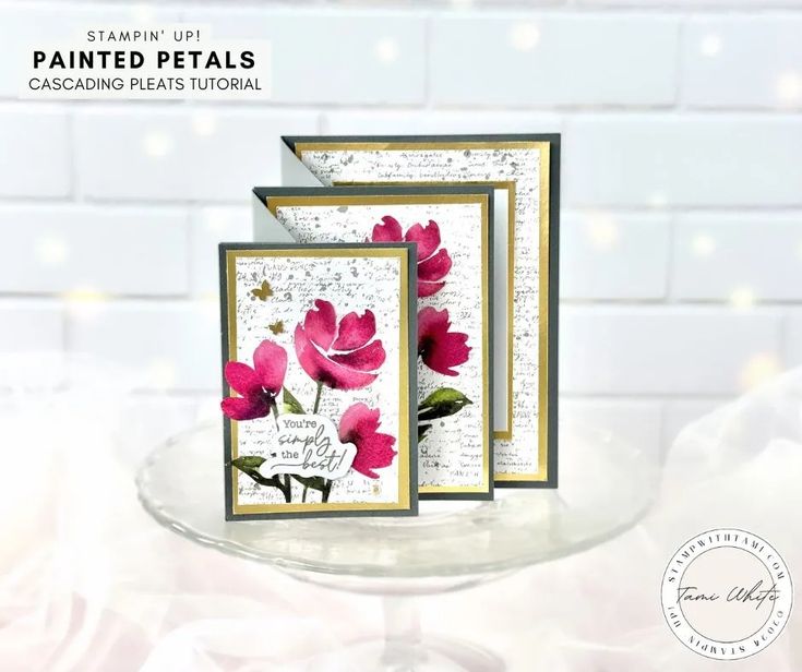 two cards with pink flowers on them sitting on a glass plate next to a white brick wall