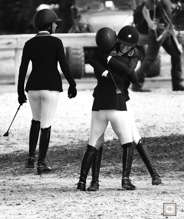 two women in riding gear standing next to each other with their backs towards one another