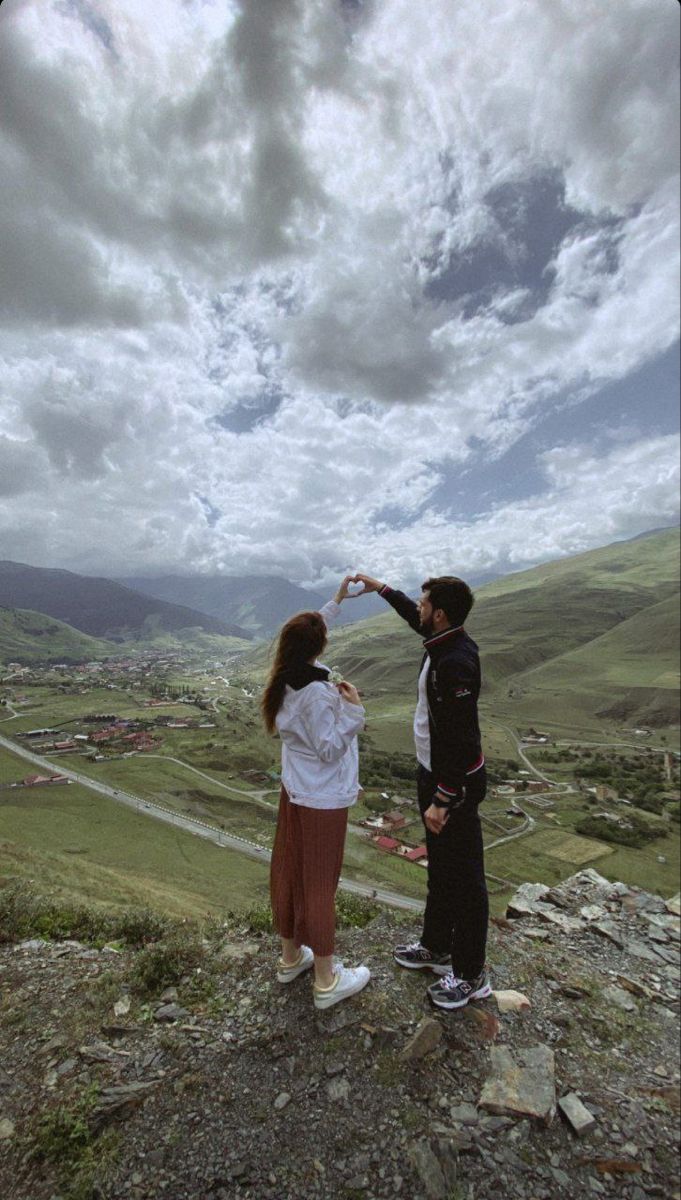 a man and woman standing on top of a hill